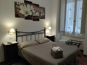 A bedroom with a bed, two bedside tables, a nightstand, a lamp, a window with curtains, and a wall-mounted artwork. - Napolipietrasanta LT (Naples)