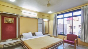 Quarto de hotel com uma cama grande, uma cadeira vermelha, uma janela com cortinas e um quadro na parede.