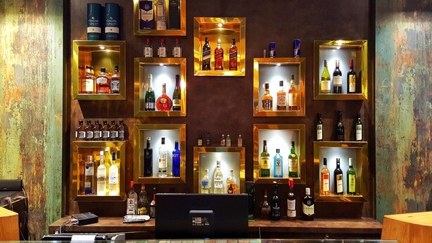 Uma área de bar com várias prateleiras exibindo diferentes garrafas de bebidas.