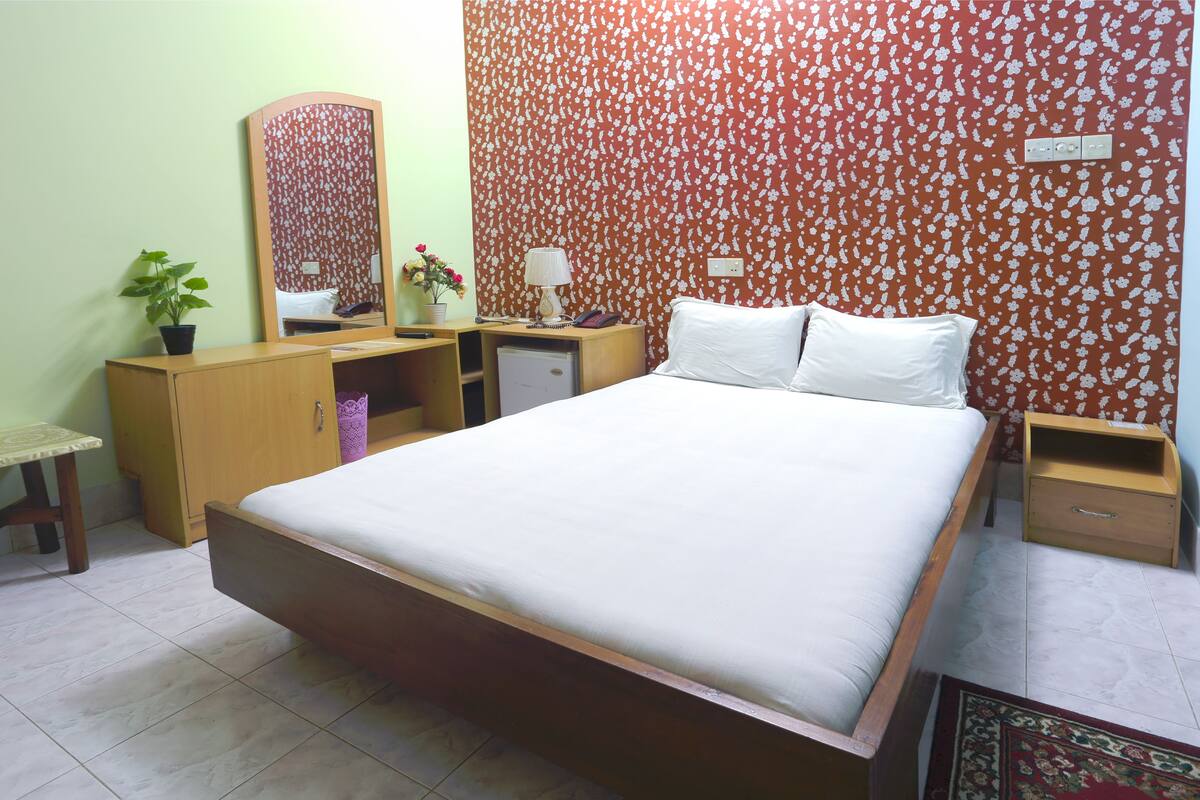A bedroom with a large bed, wooden nightstands, a dresser, a mirror, and a floral-patterned wall.