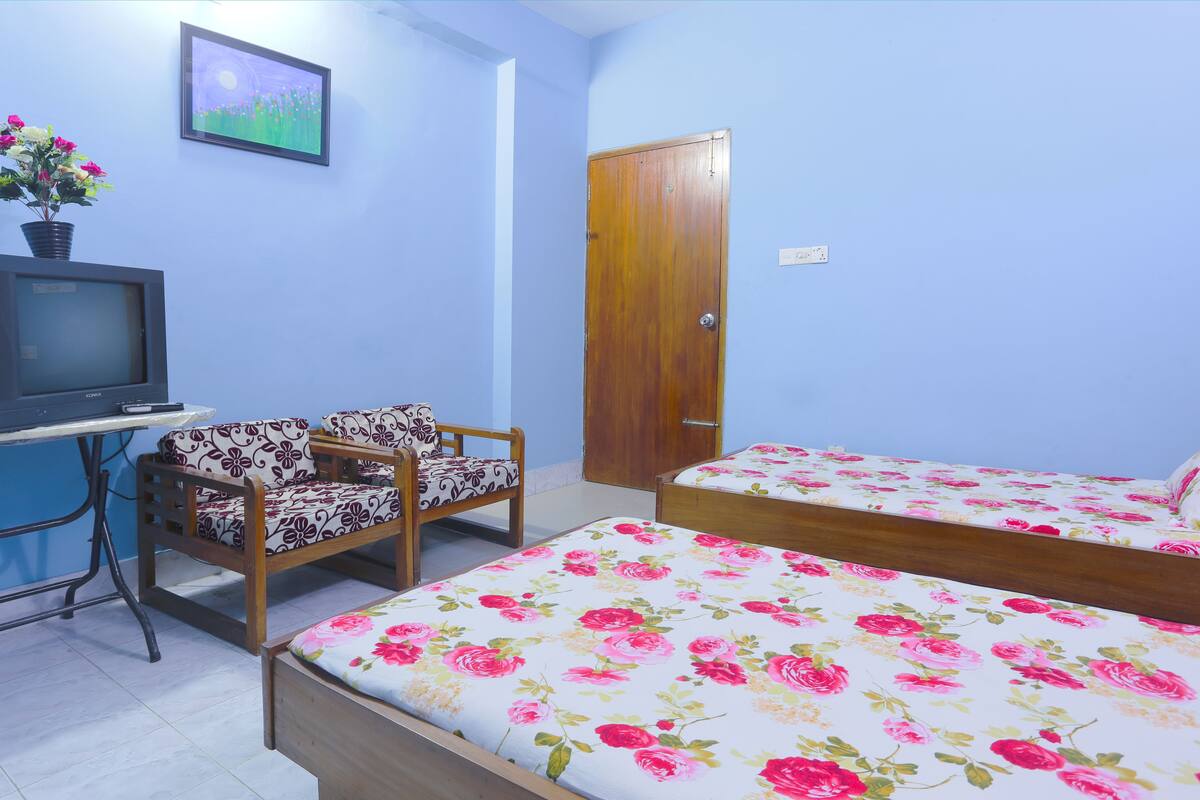 A bedroom with two single beds, a wooden wardrobe, a small table with a TV, and a chair.