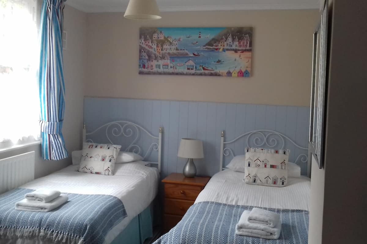 A bedroom with two beds, a nightstand, a lamp, and a painting of a coastal scene.