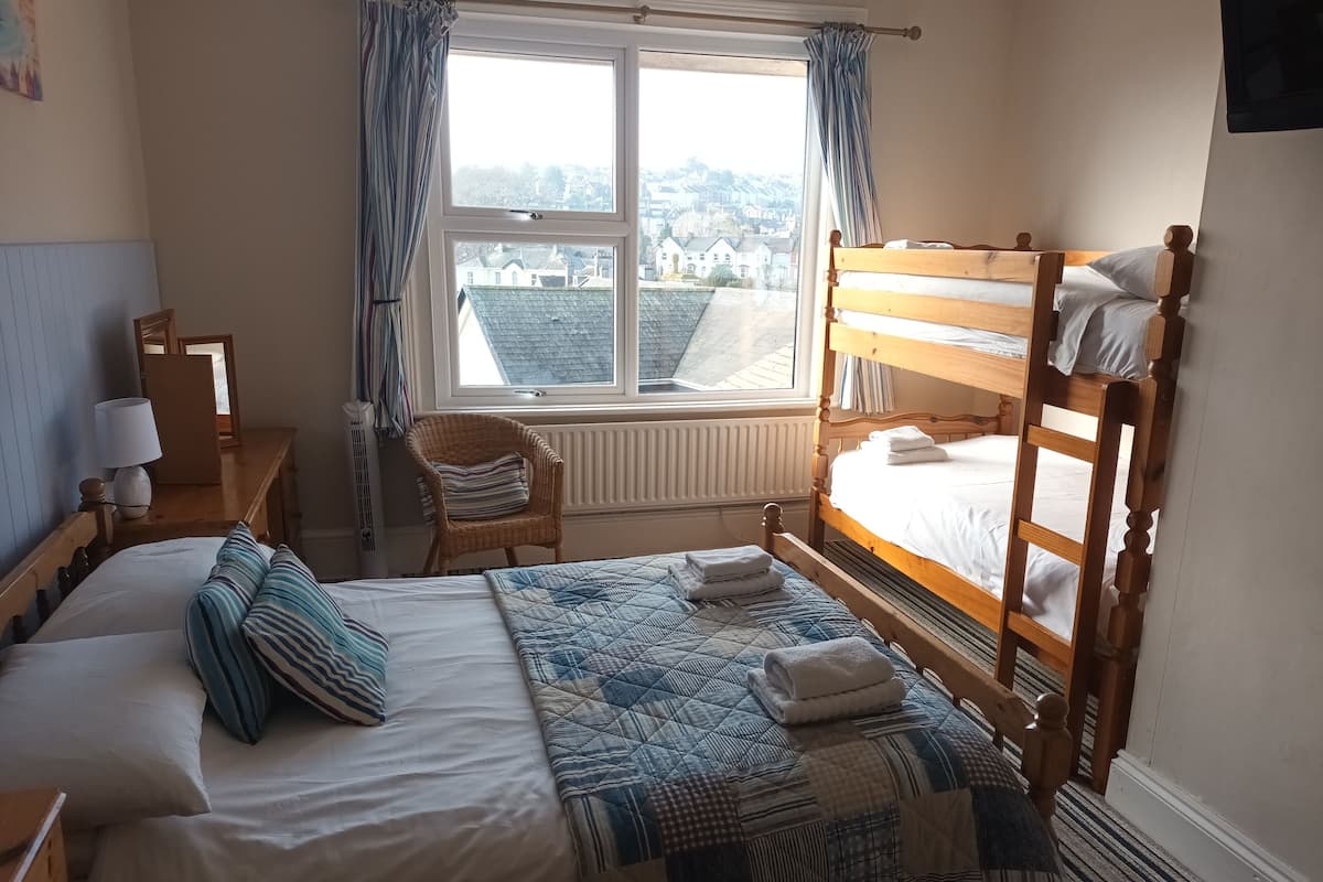 A bedroom with a bunk bed, a single bed, a chair, a radiator, and a window with curtains.