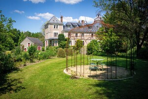 Une grande maison avec un jardin, un belvédère et une table entourée de chaises.