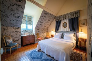 Une chambre avec un grand lit, une commode, une chaise et une fenêtre.