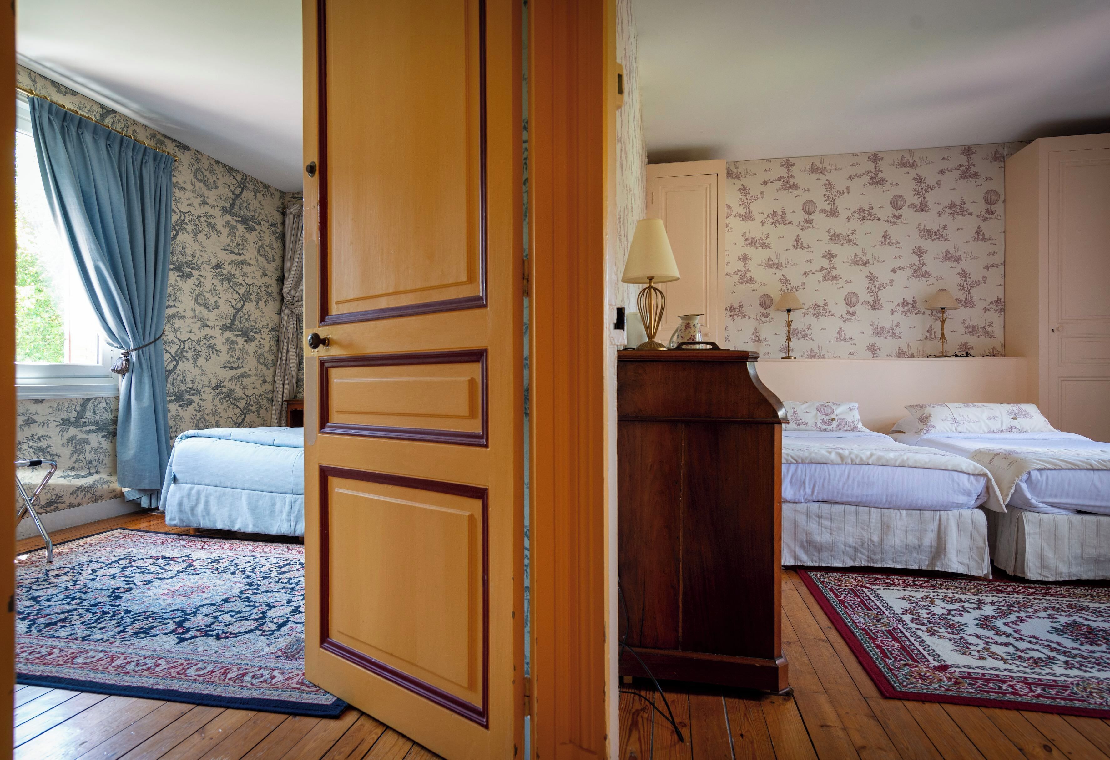 Un dormitorio con dos camas, una puerta de madera y una ventana con cortinas azules.
