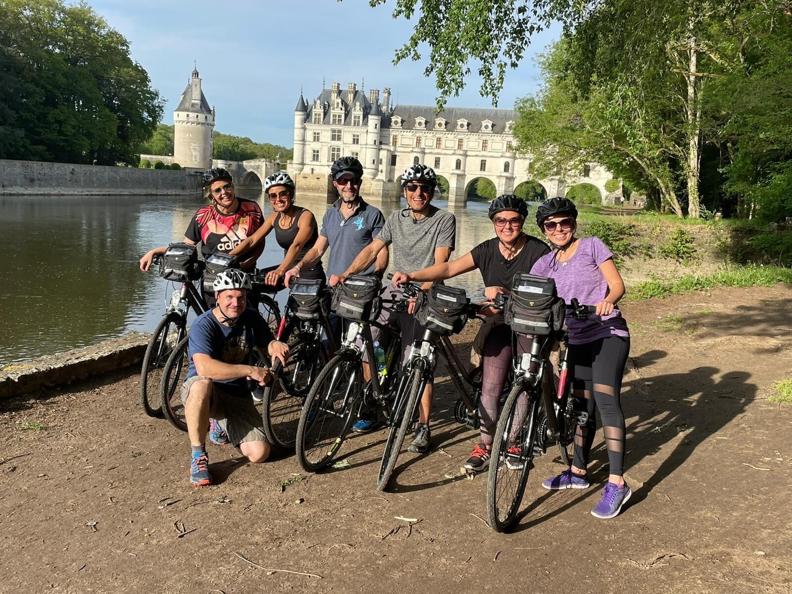 Un groupe de personnes à vélo se trouve près d’un bâtiment historique, au bord d’un plan d’eau.
