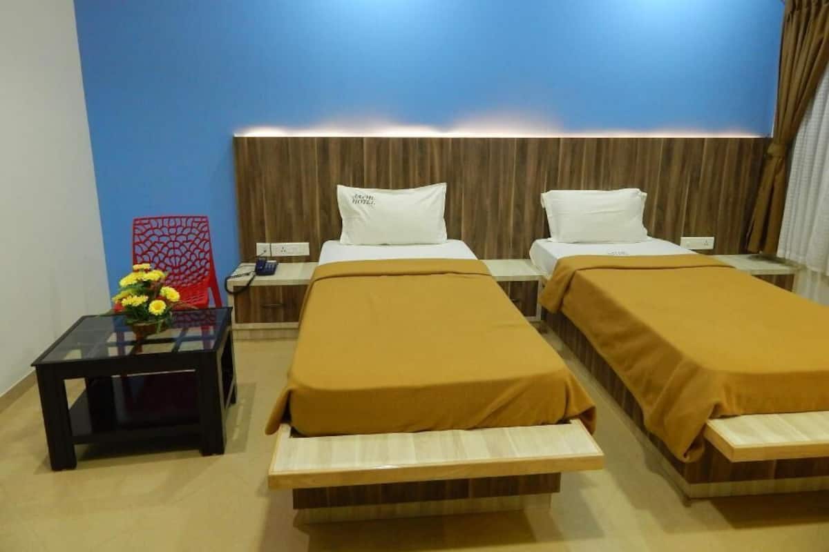 A hotel room with two single beds, a small table with a vase of flowers, and a red chair.