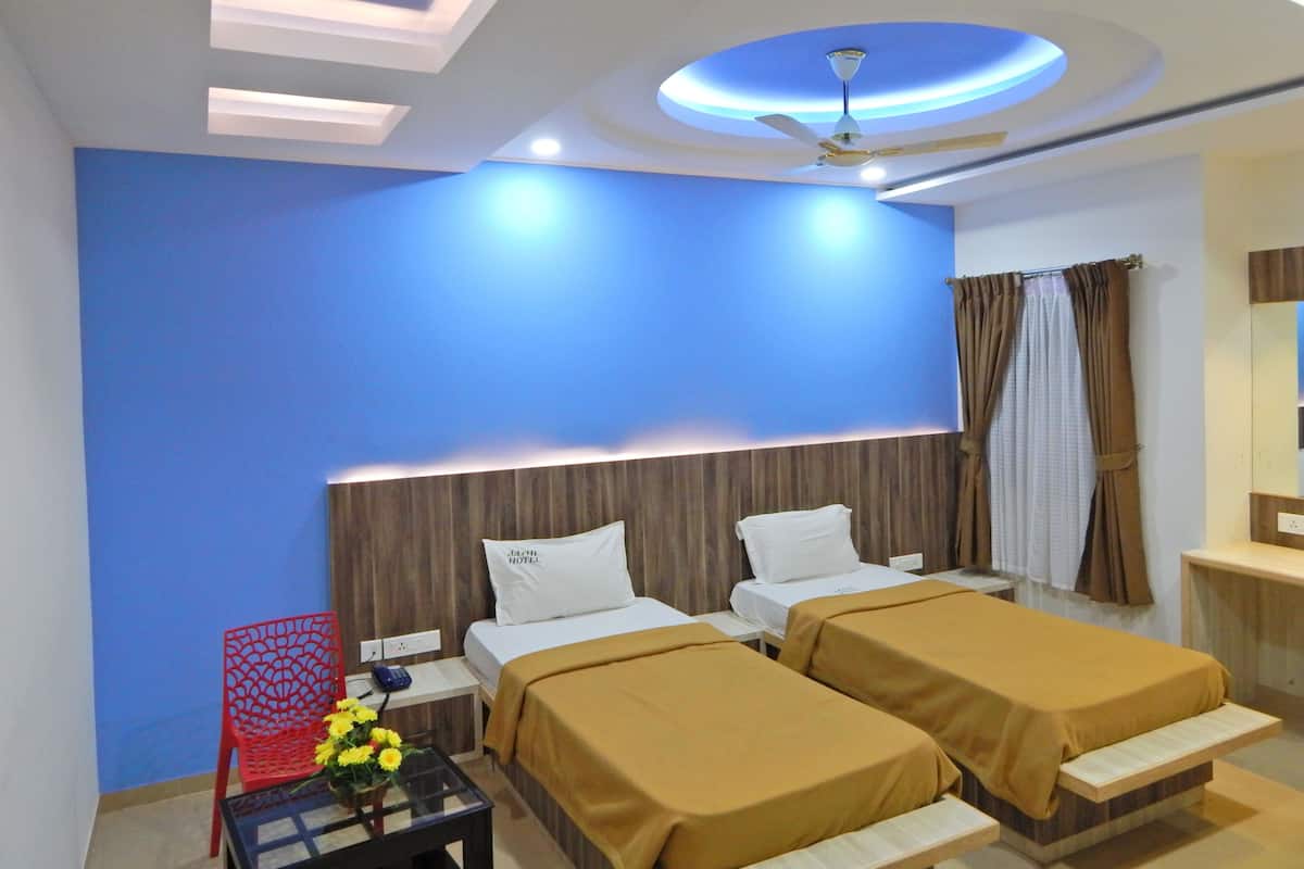 A hotel room with two beds, a red chair, a small table with flowers, and a ceiling fan.