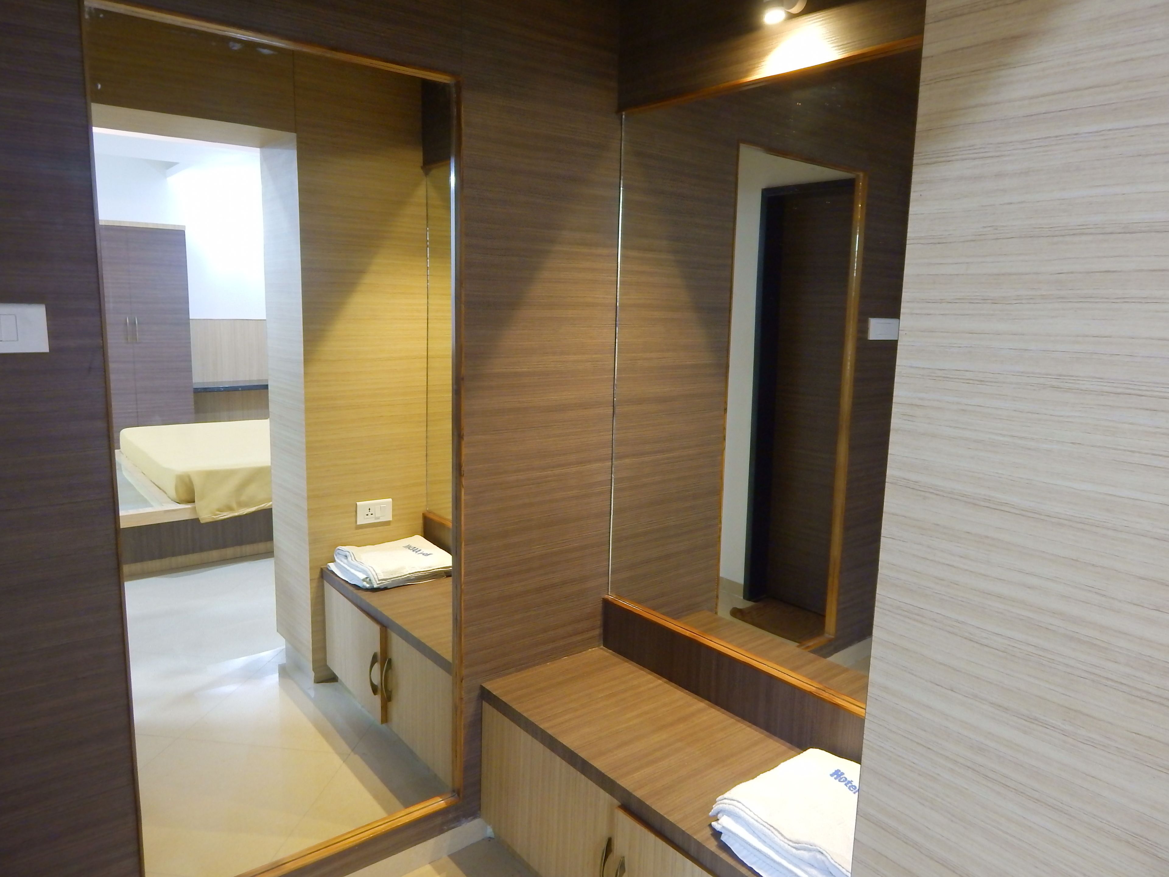 Habitación de hotel con tocador de madera, un espejo, una cama con colcha amarilla y una toalla blanca doblada en el mostrador.