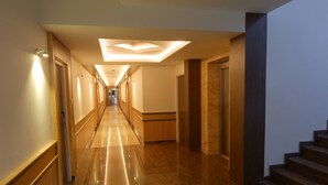 A long, well-lit hallway with a shiny floor, leading to a staircase. - Hotel Aadhi (Mayiladuthurai)