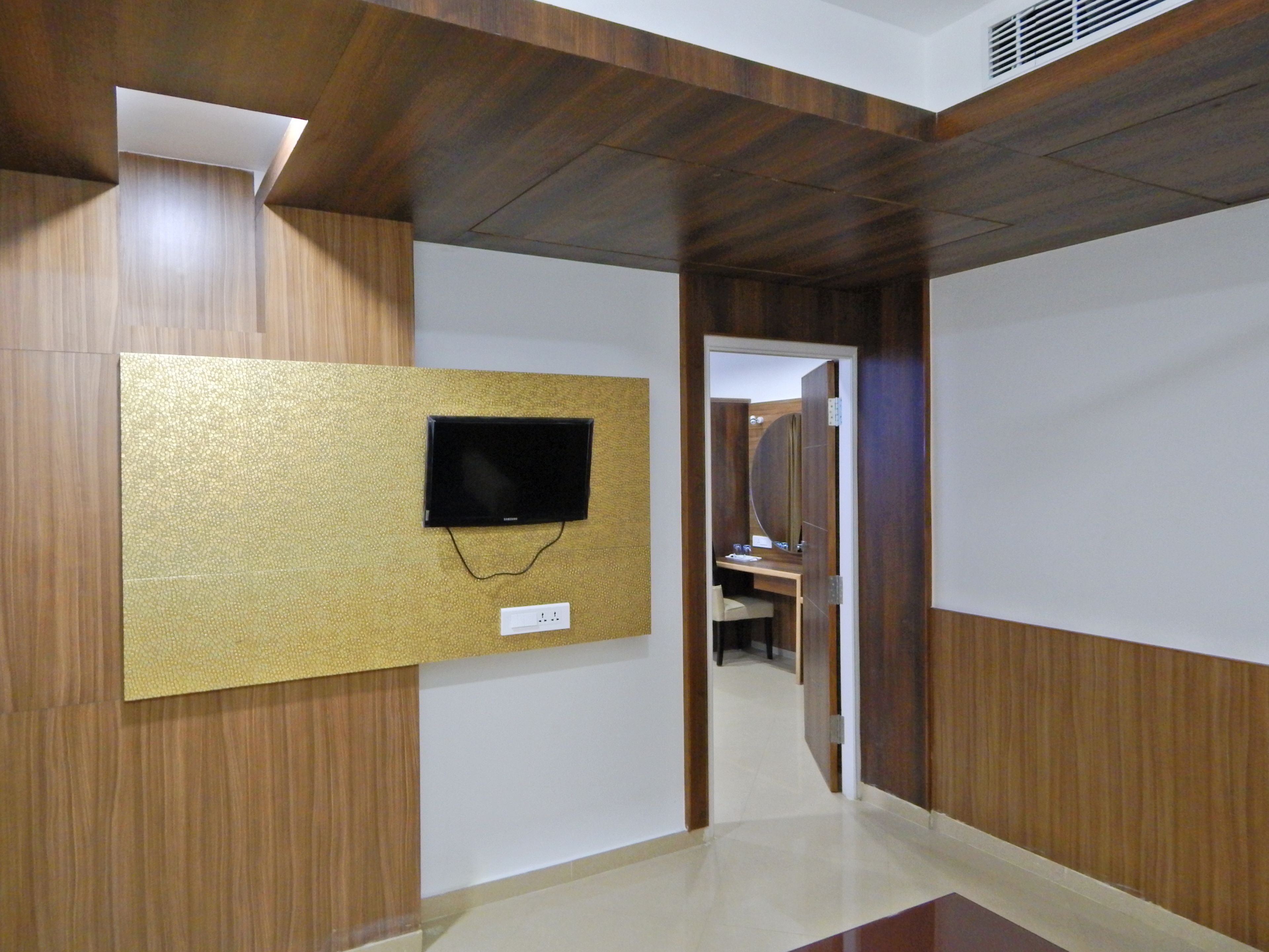 Un pasillo con paneles de madera, un televisor montado y un espejo que refleja un baño con lavamanos y espejo.