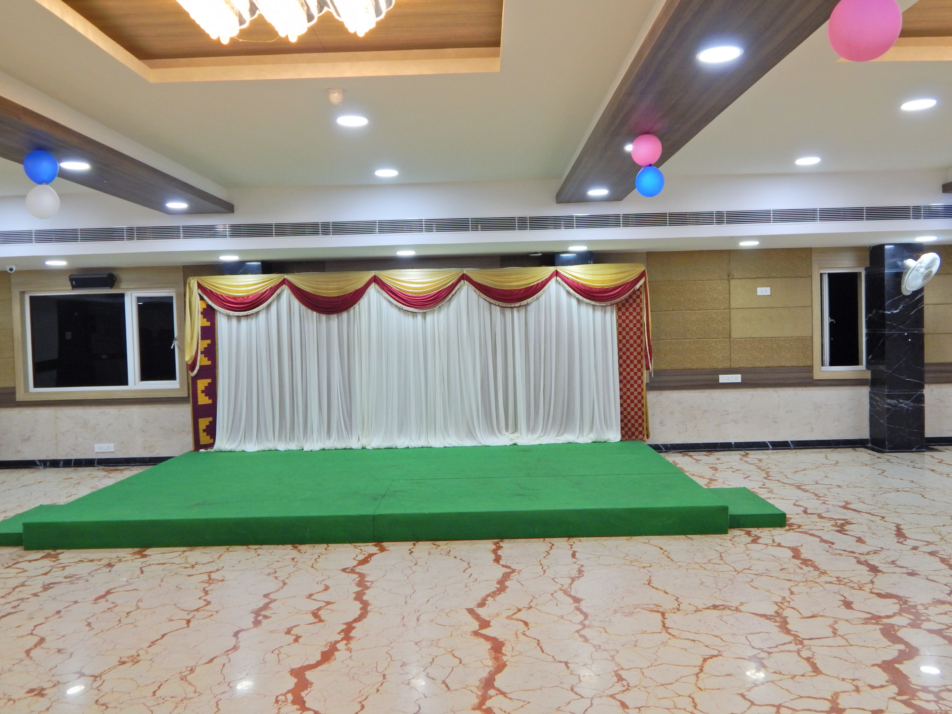 Un escenario con alfombra verde, cortinas drapeadas y pared con estampado de cuadros.