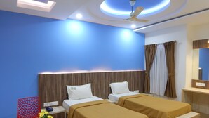 A hotel room with two beds, a red chair, a small table with a vase of flowers, and a ceiling fan. - Hotel Aadhi (Mayiladuthurai)