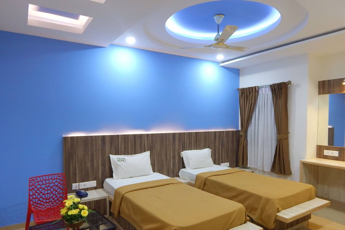 A hotel room with two beds, a red chair, a small table with a vase of flowers, and a ceiling fan.