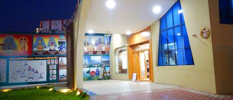 A building with a tiled entrance, a grassy area, and a poster with images and text.