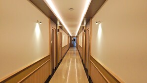 A long, well-lit hallway with wooden paneling and doors on both sides, leading to a room at the end. - Hotel Aadhi (Mayiladuthurai)