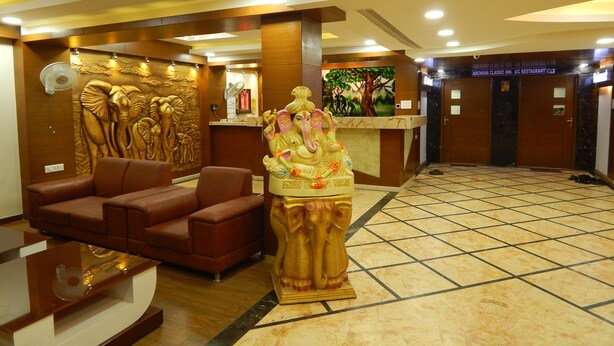 A reception area with a statue, a reception desk, a brown sofa, and a tiled floor. - Hotel Aadhi (Mayiladuthurai)