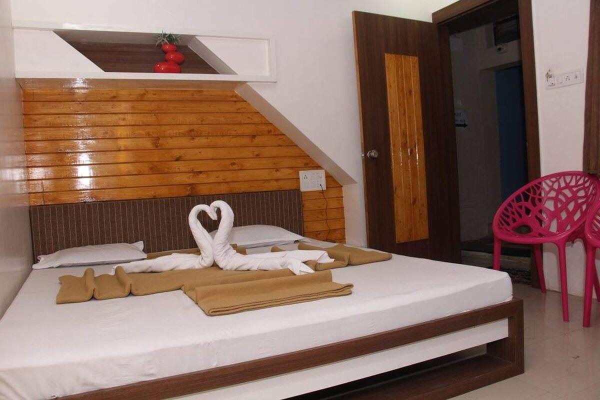 A neatly made bed with a wooden headboard, a heart-shaped towel arrangement, and a pink chair in the corner.