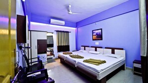 A hotel room with a large bed, a ceiling fan, an air conditioner, and a television. - Hotel Royal (Diu)