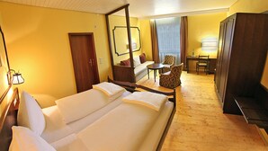 Quarto de hotel com uma cama grande, área de estar com sofá e poltronas, escrivaninha e guarda-roupa.