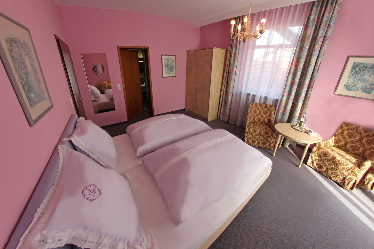 Habitación de hotel en tonos rosados, con una cama grande, una mesita redonda pequeña y un sofá.