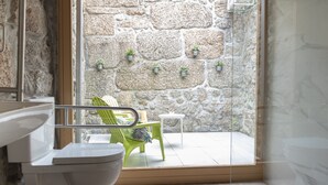 Un baño con pared de piedra, techo de madera y vistas a un espacio exterior con mesa y sillas.