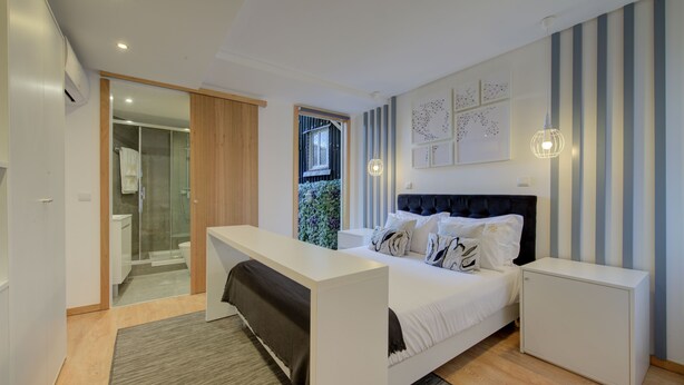 Un dormitorio moderno con cama, mesitas de noche, escritorio y zona de ducha.