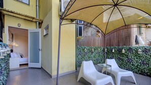 Un patio con una pared amarilla, una puerta blanca y una zona de estar bajo un toldo.
