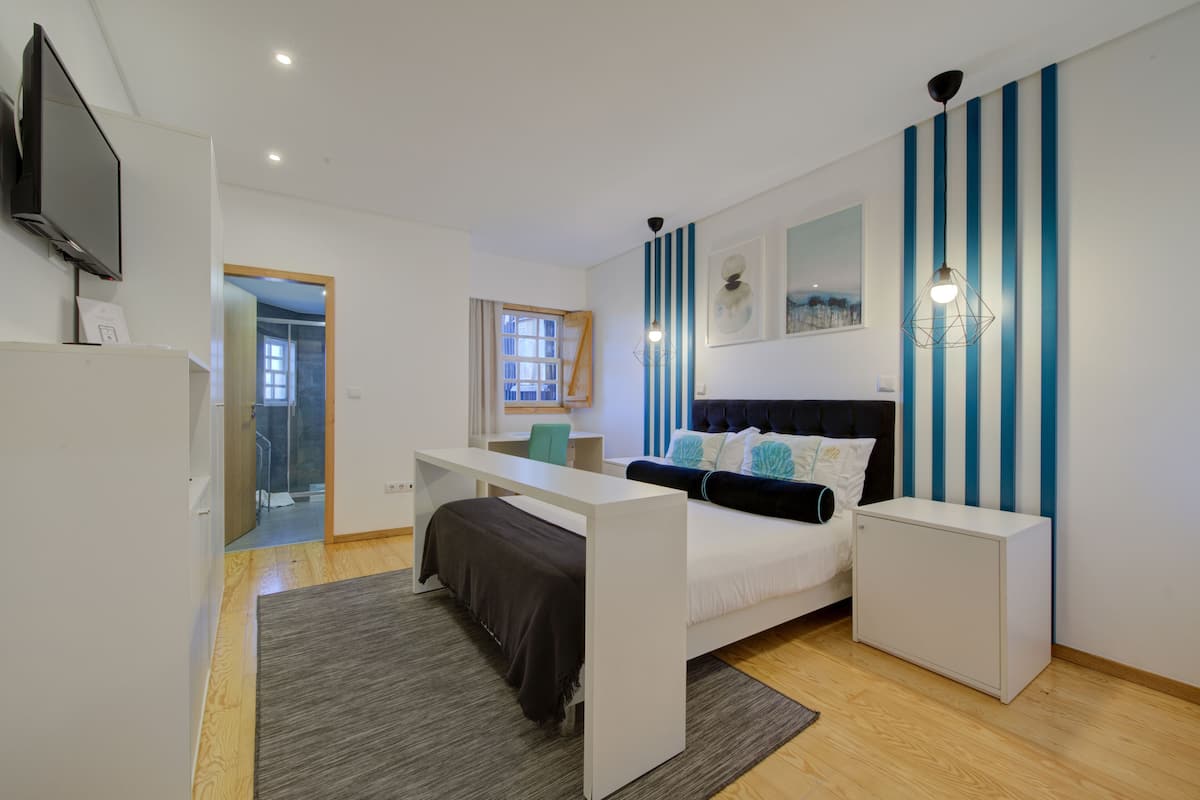 A modern bedroom with a bed, a desk, a TV, and a window.