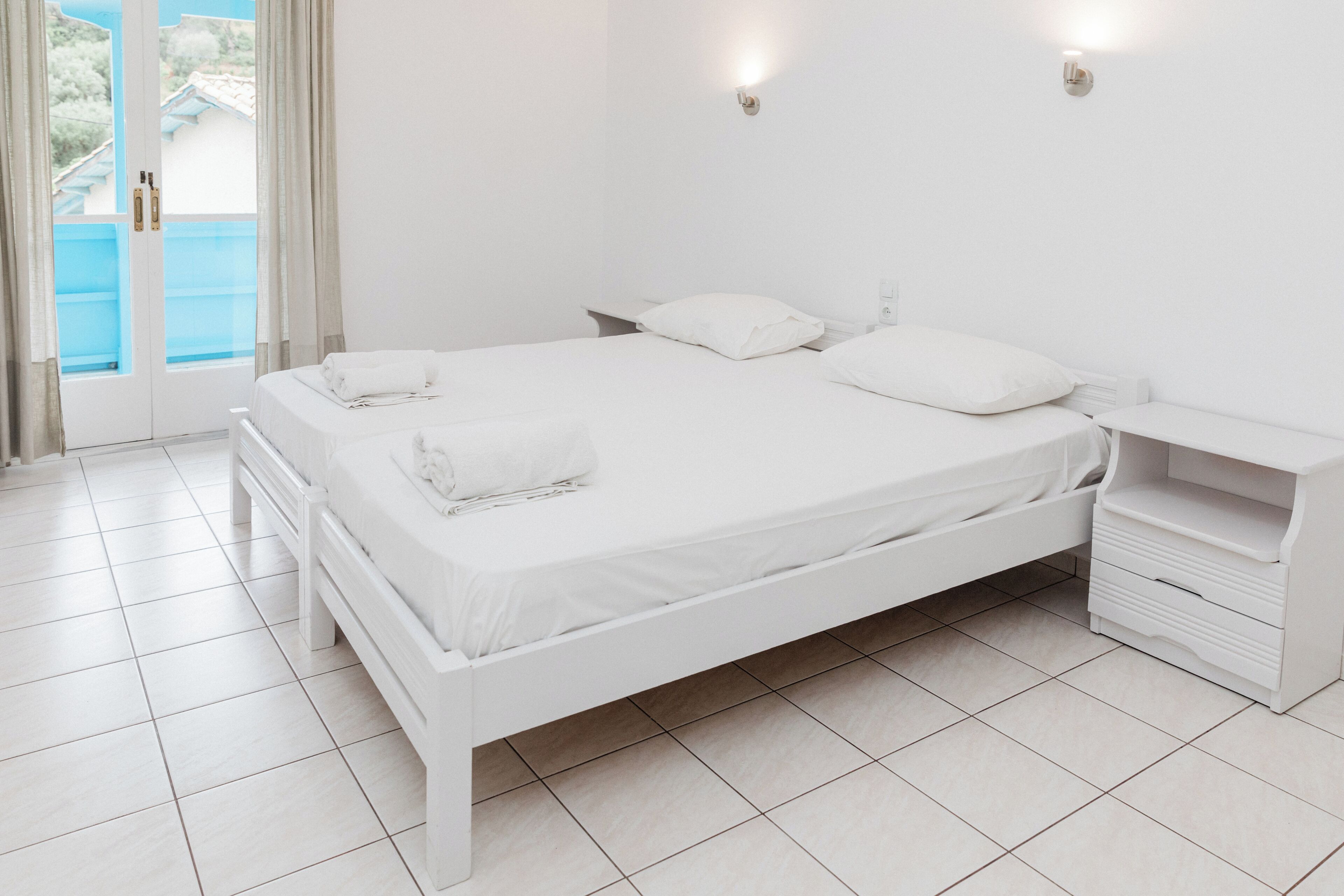 A white bedroom with a bed, bedside tables, and a view through a glass door.