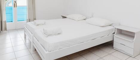 A white bedroom with a bed, bedside tables, and a view through a glass door.
