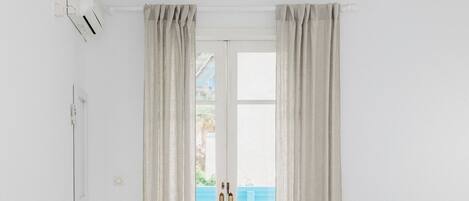 Habitación de hotel minimalista con cama, escritorio pequeño y ventana con cortinas.