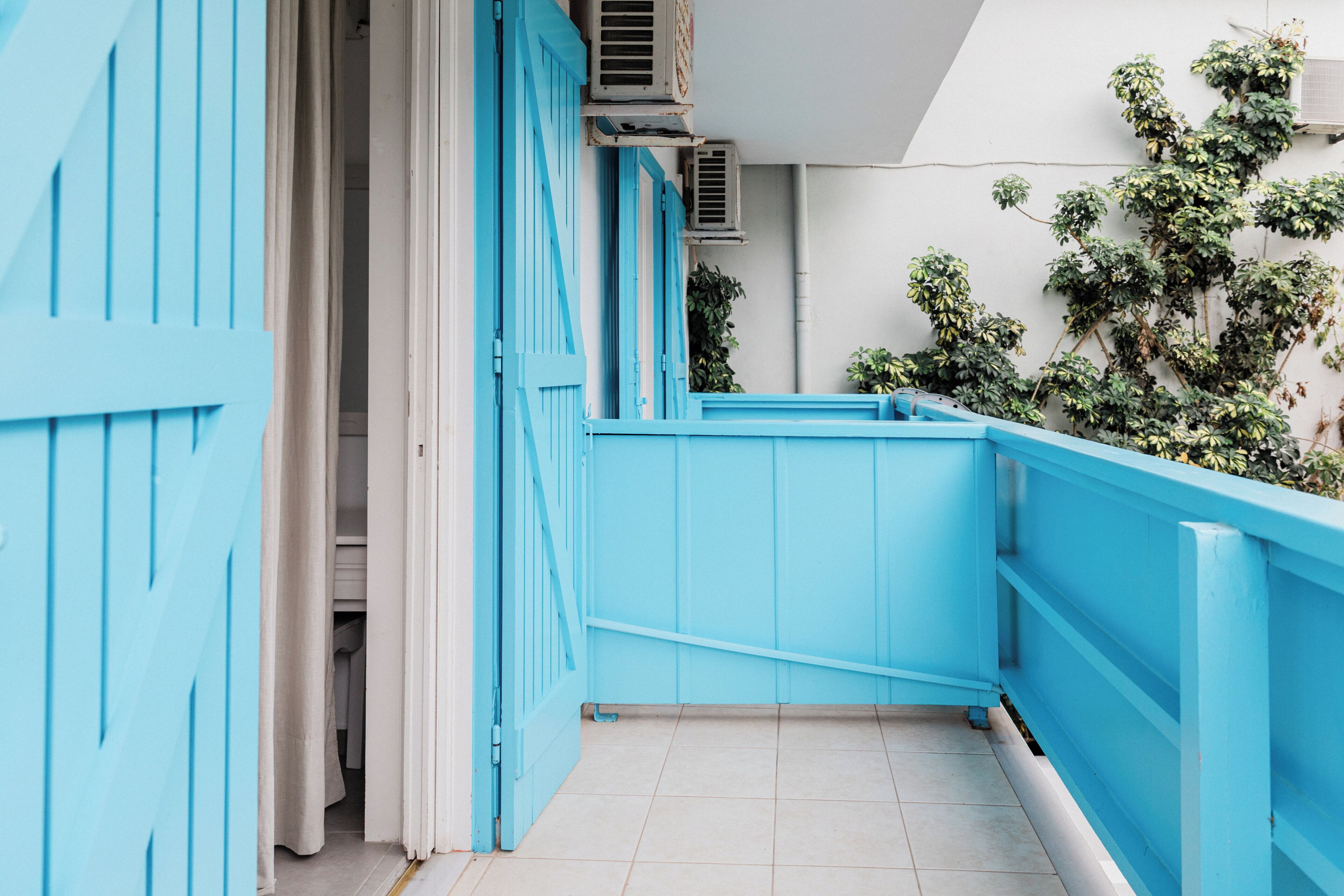 A narrow corridor with a blue door and a blue railing, leading to a room with a white ceiling and a green plant.