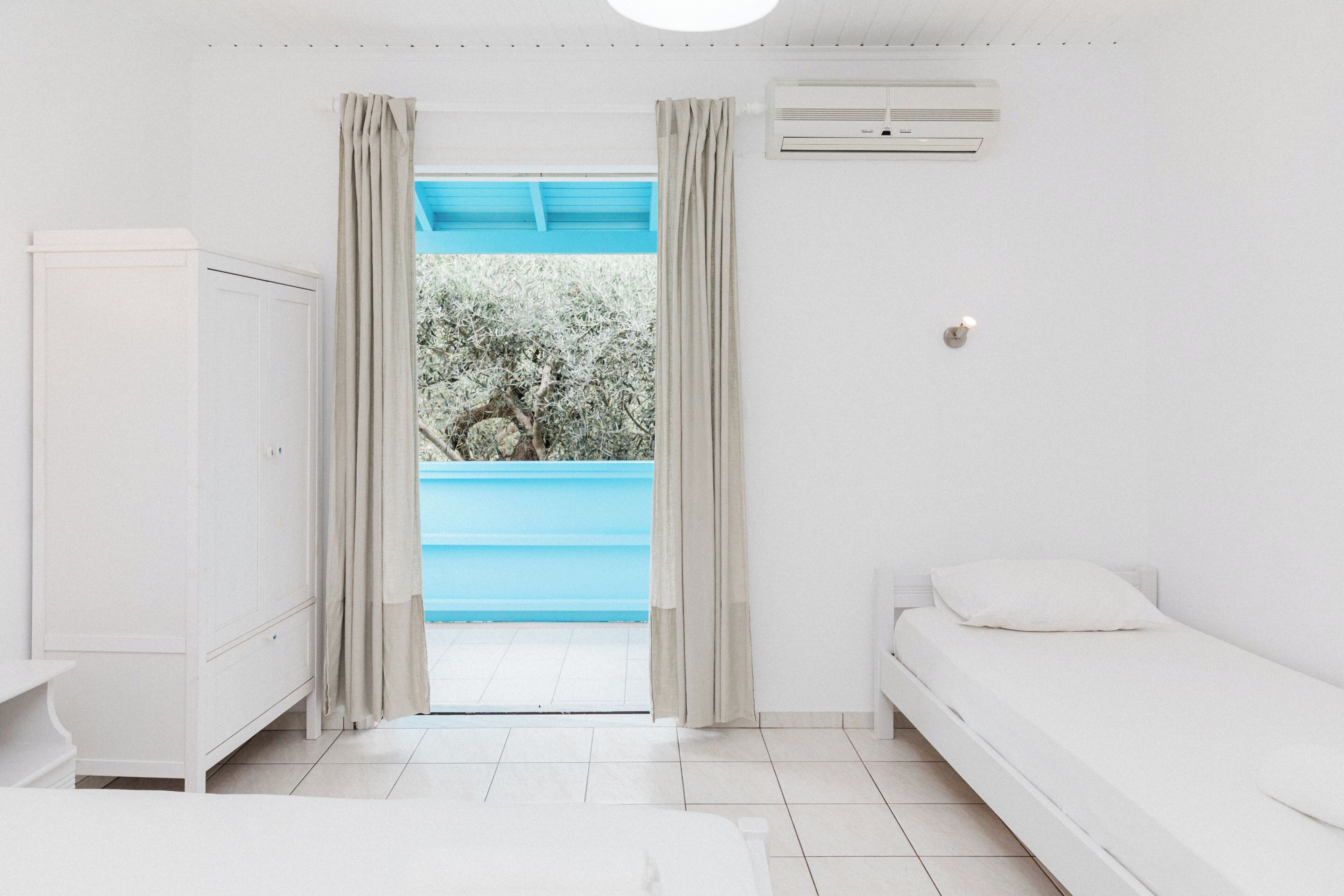 Une chambre avec un lit, une armoire, un appareil de climatisation et une vue sur une piscine bleue.