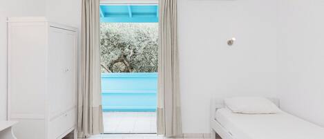 Un dormitorio con cama, armario, aire acondicionado y vistas a una piscina azul.