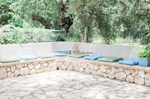 Un área de estar al aire libre con paredes de piedra, una mesa de vidrio y bancos acolchados.