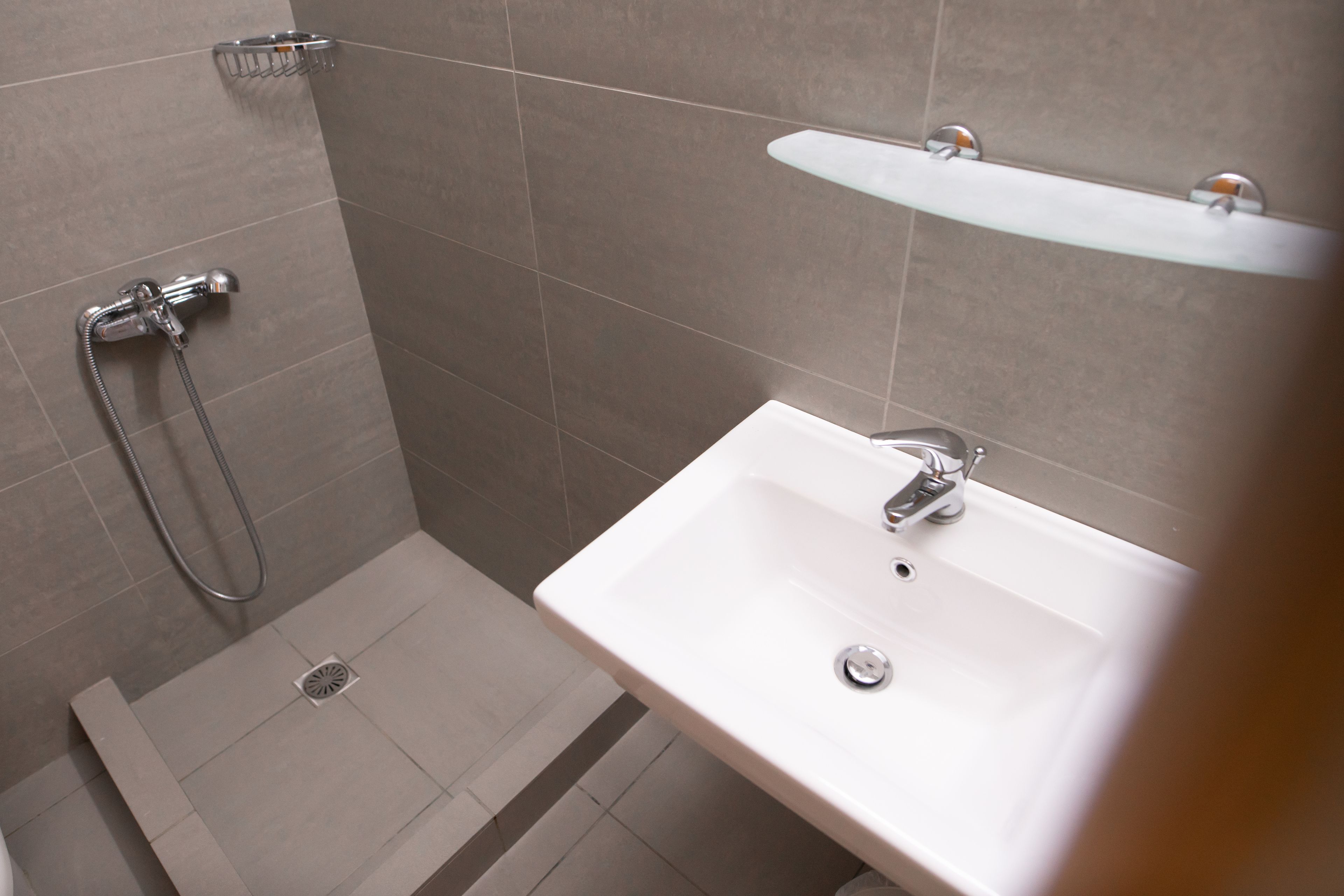 A bathroom with a shower, sink, and a glass shelf.