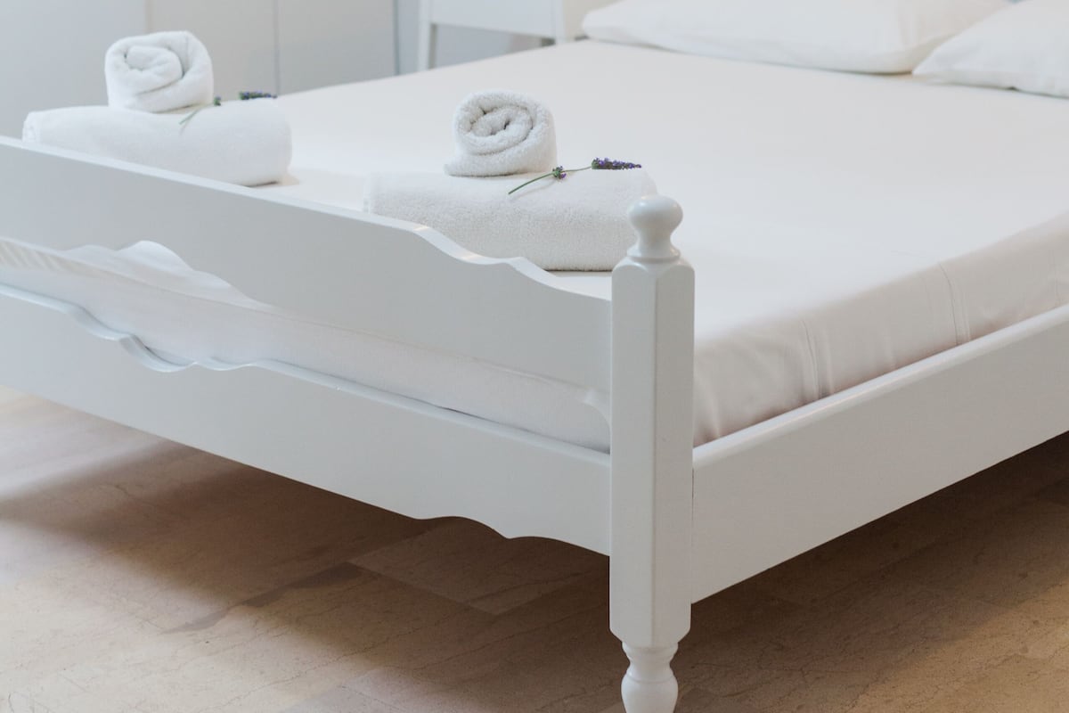 A white, single-bed room with a wooden headboard, a bedside table, and a nightstand.