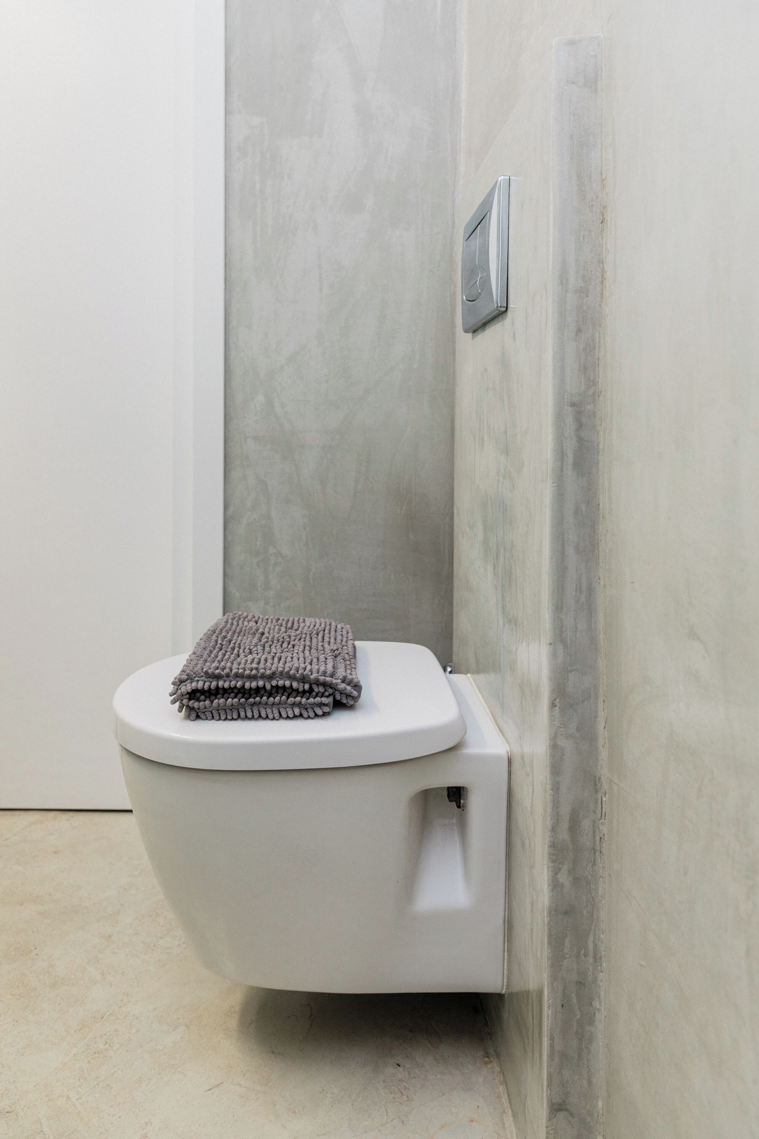 A modern toilet with a white seat and lid, positioned against a textured grey wall.