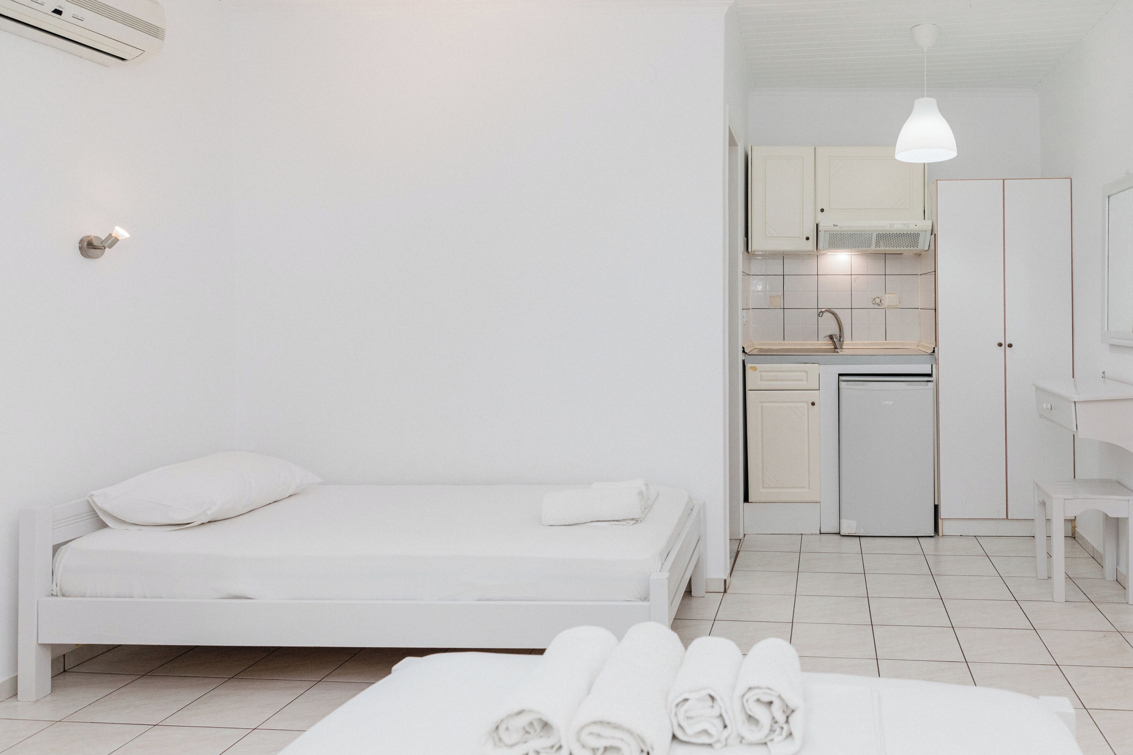 Una habitación minimalista con cama, kitchenette pequeña y baño.