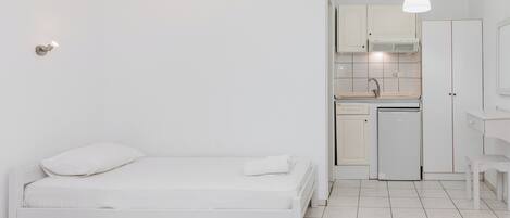 Una habitación minimalista con cama, kitchenette pequeña y baño.