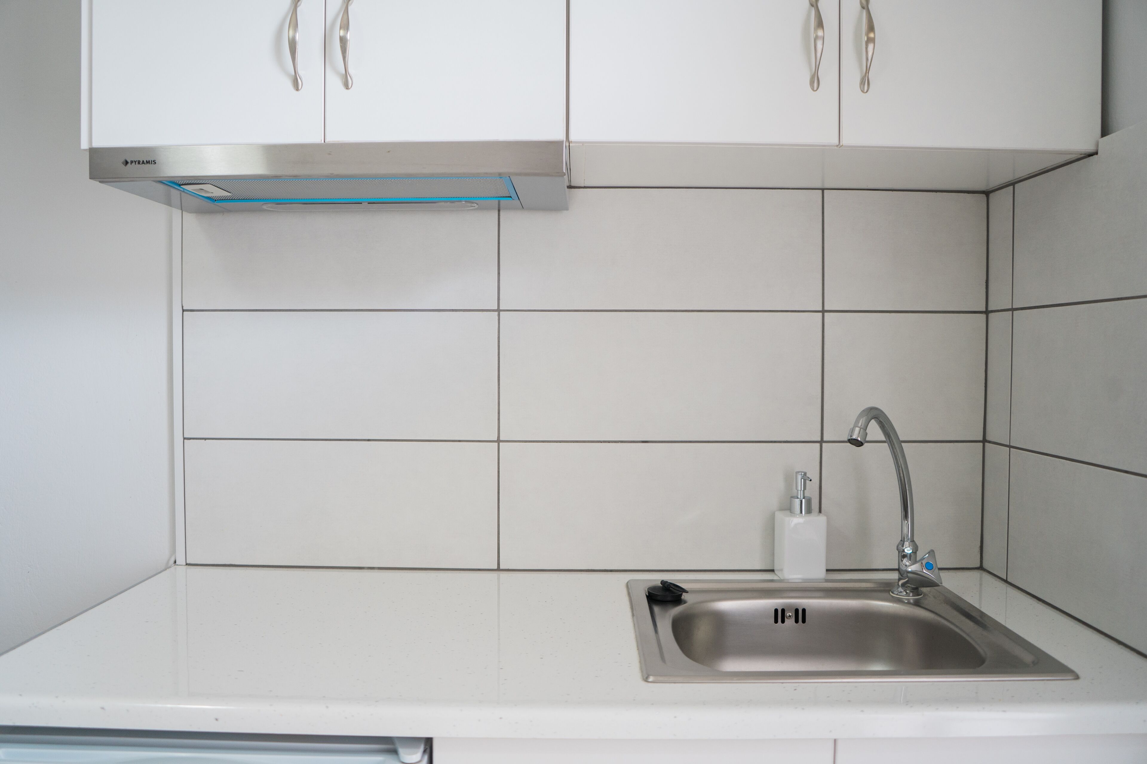 A kitchen with white cabinets, a stainless steel sink, and a built-in range hood.