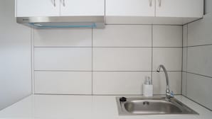 A kitchen with white cabinets, a stainless steel sink, and a built-in range hood. - Afroditi Pansion (Lefkada)