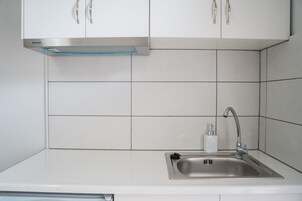 Una cocina con armarios blancos, un lavamanos de acero inoxidable y una campana extractora integrada.
