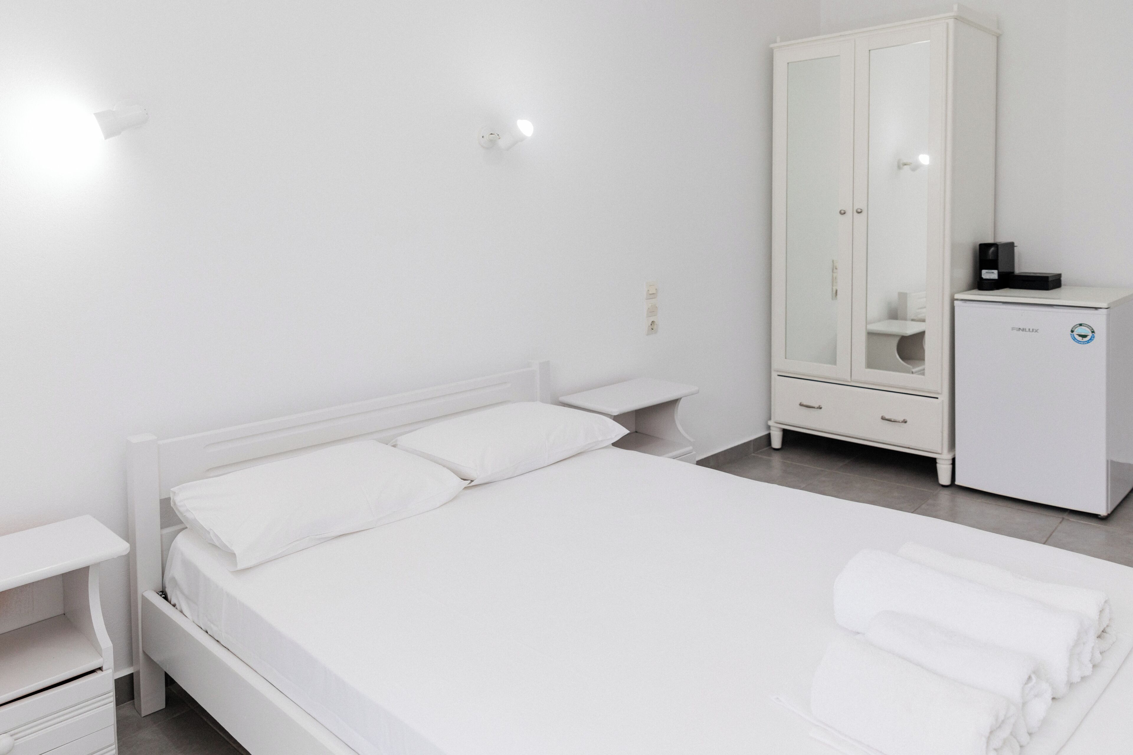 Ein helles Schlafzimmer mit einem Bett, einem Kleiderschrank und einem kleinen weißen Schrank.
