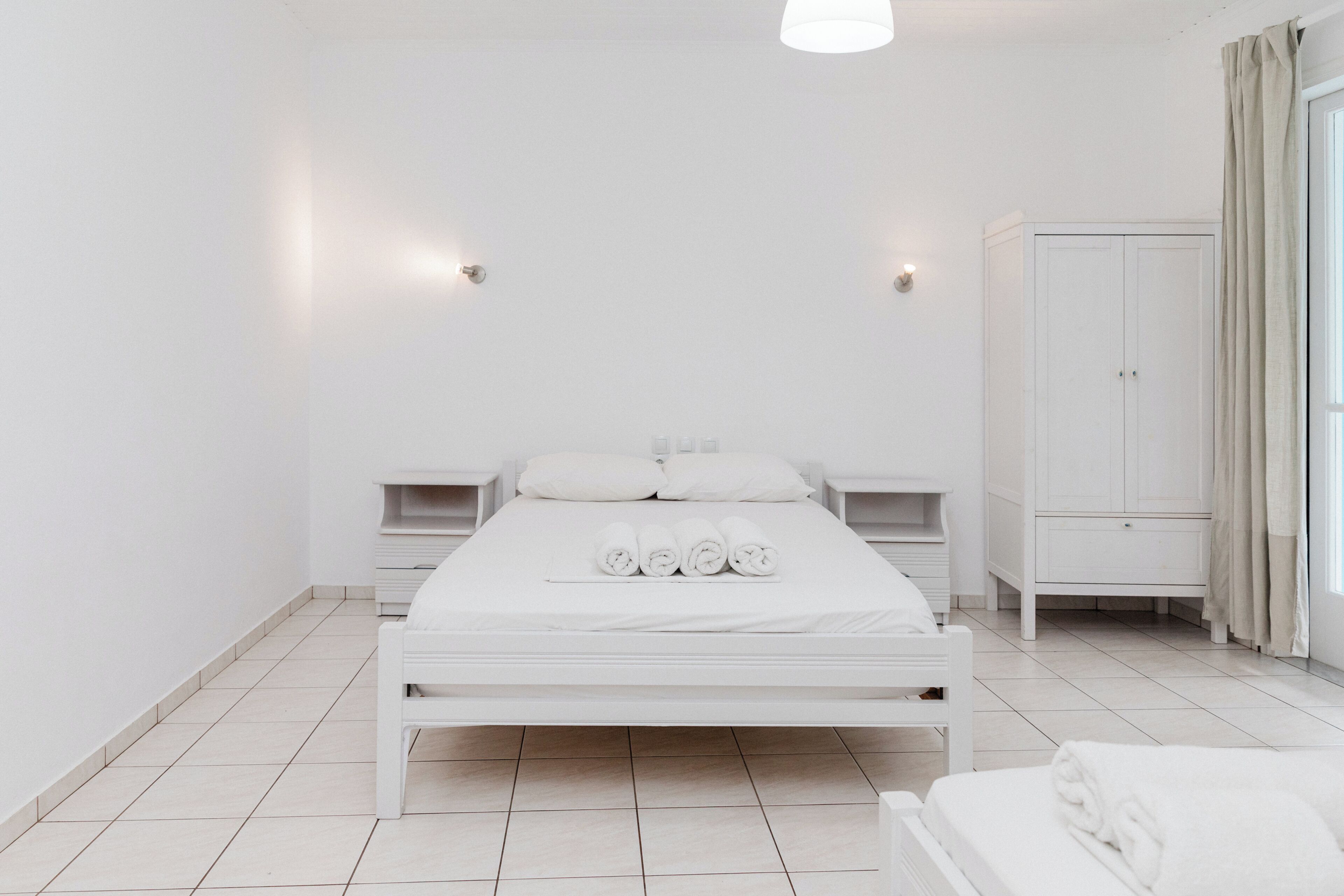 A minimalist white bedroom with a bed, bedside tables, and a wardrobe.