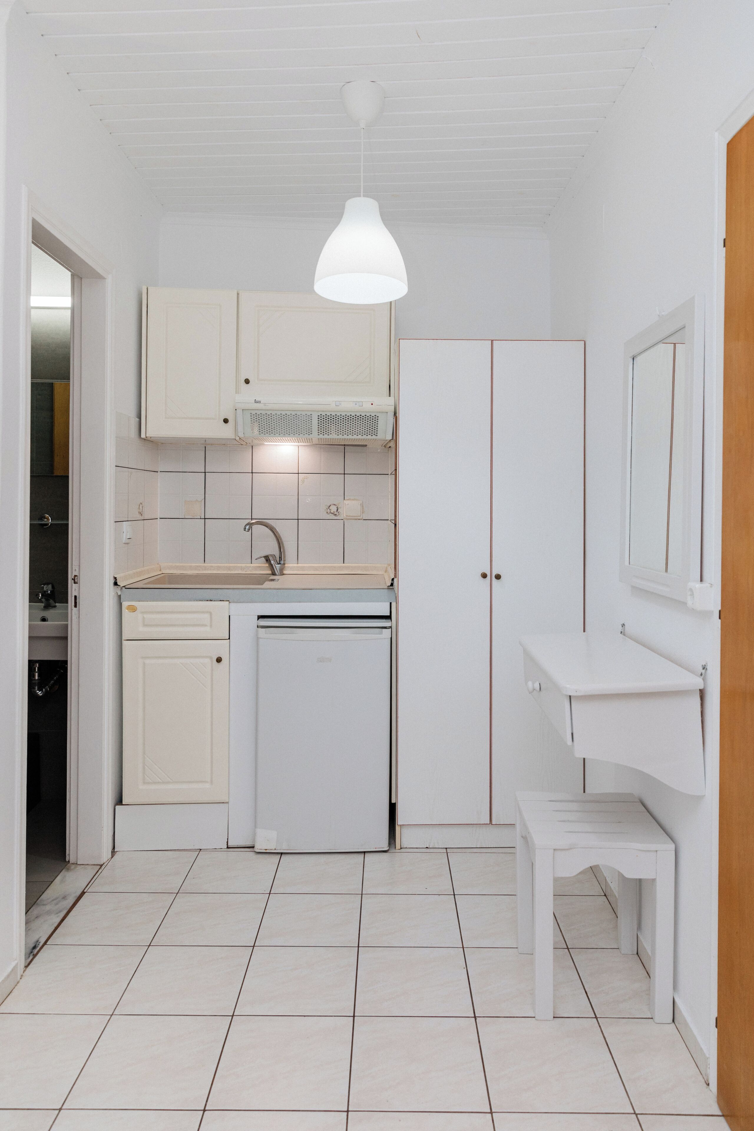 A compact kitchen with white cabinetry, a built-in oven, and a hanging pendant light.