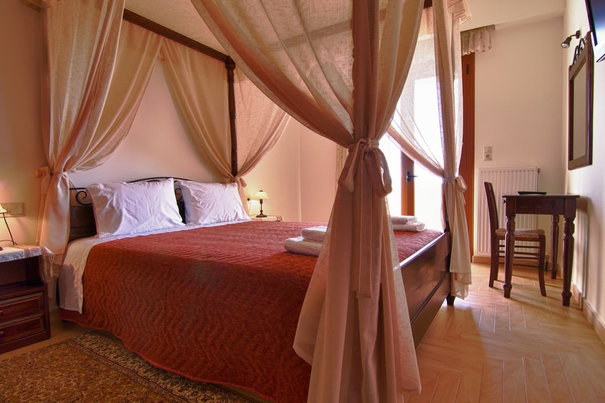A bedroom with a four-poster bed, a wooden desk, and a chair.
