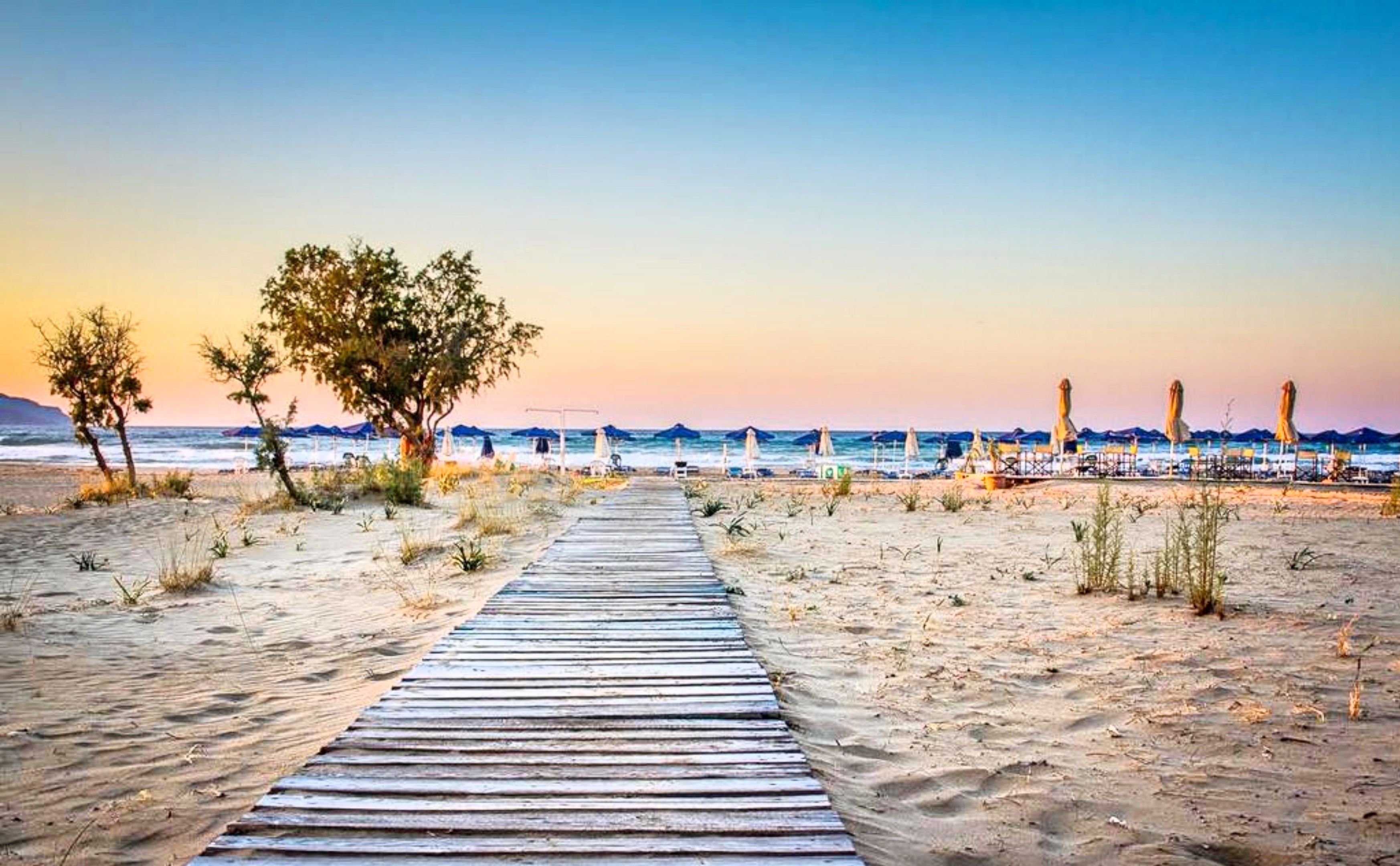 A wooden pathway leading to a beach with umbrellas and lounge chairs.
